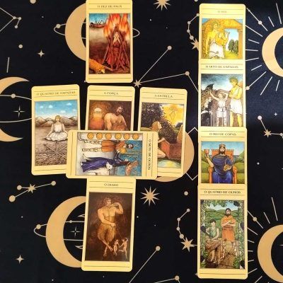 A foto apresenta um jogo de 10 cartas com o tarô mitológico, sendo do lado esquerdo 6 cartas em formato de cruz a à direita, 4 cartas em linha vertical. As cartas possuem um tom amarelo citrino e ilustrações de alto contraste com os elementos da mitologia grega.